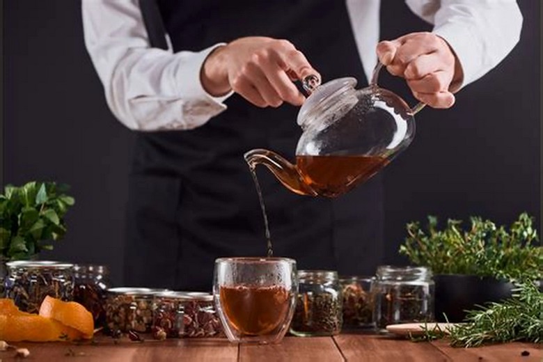 Người pha rót trà đen vào cốc thủy tinh nhỏ với lá bạc hà